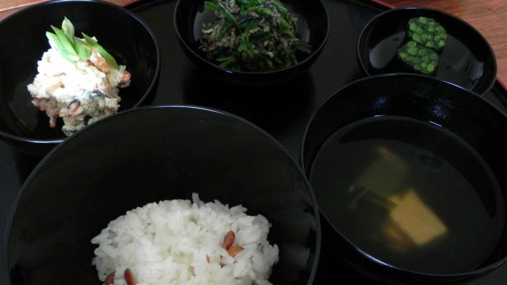 応量器(じはつ)の五つ椀。入れ子になった黒い椀と、ご飯・汁物・副菜が並ぶ