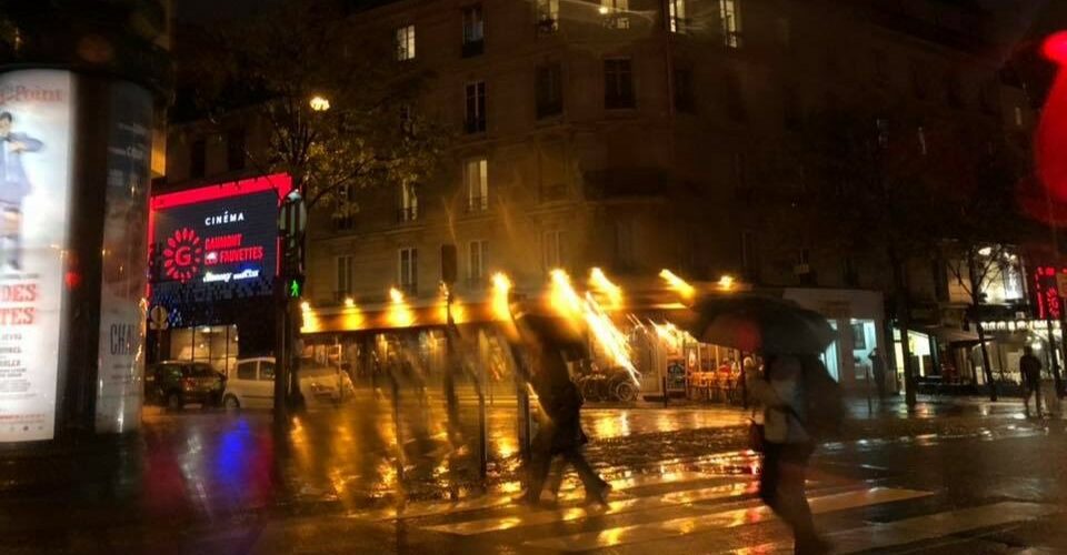 雨に濡れたパリの夜の交差点を傘をさして渡る人々