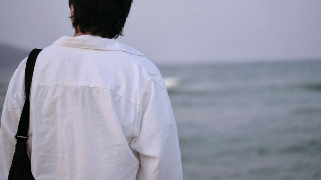 夏にHYOUGEをまとう白シャツの男性の後ろ姿と静かな海