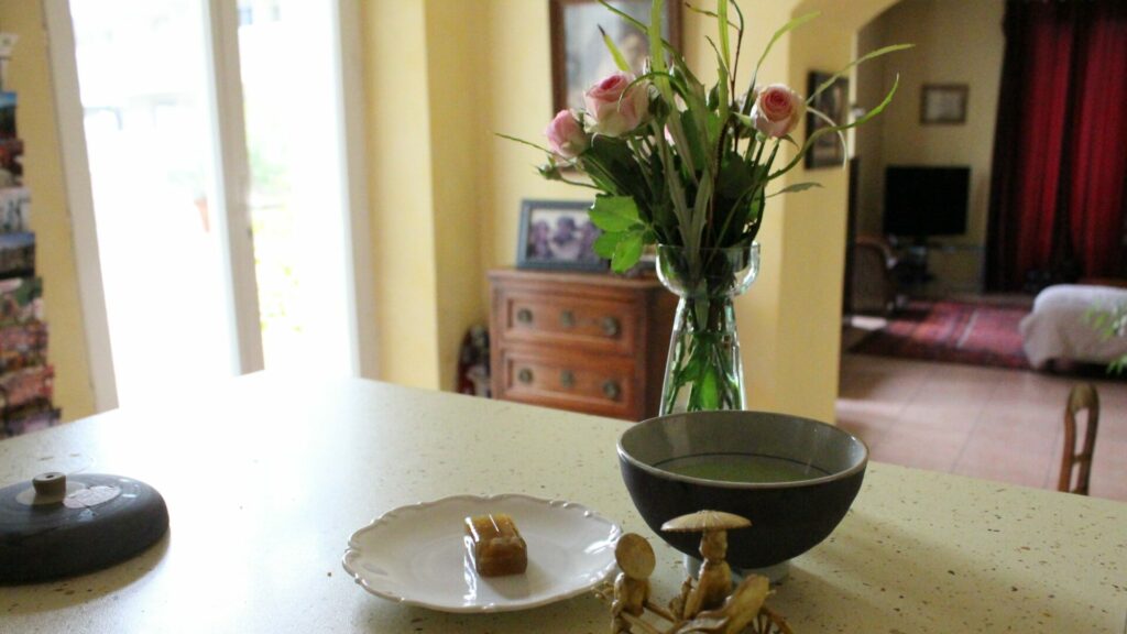 黄色い壁の南仏の部屋、テーブルに抹茶の入った黒い茶碗とバラの花