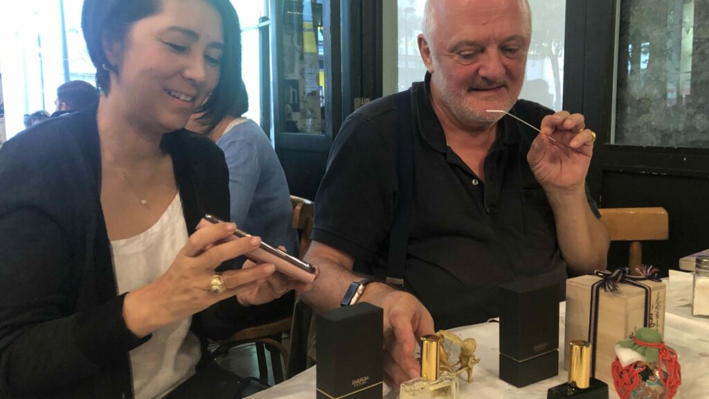 カフェのテーブルでHYOUGEを試香する男性と、隣で見守る調香師